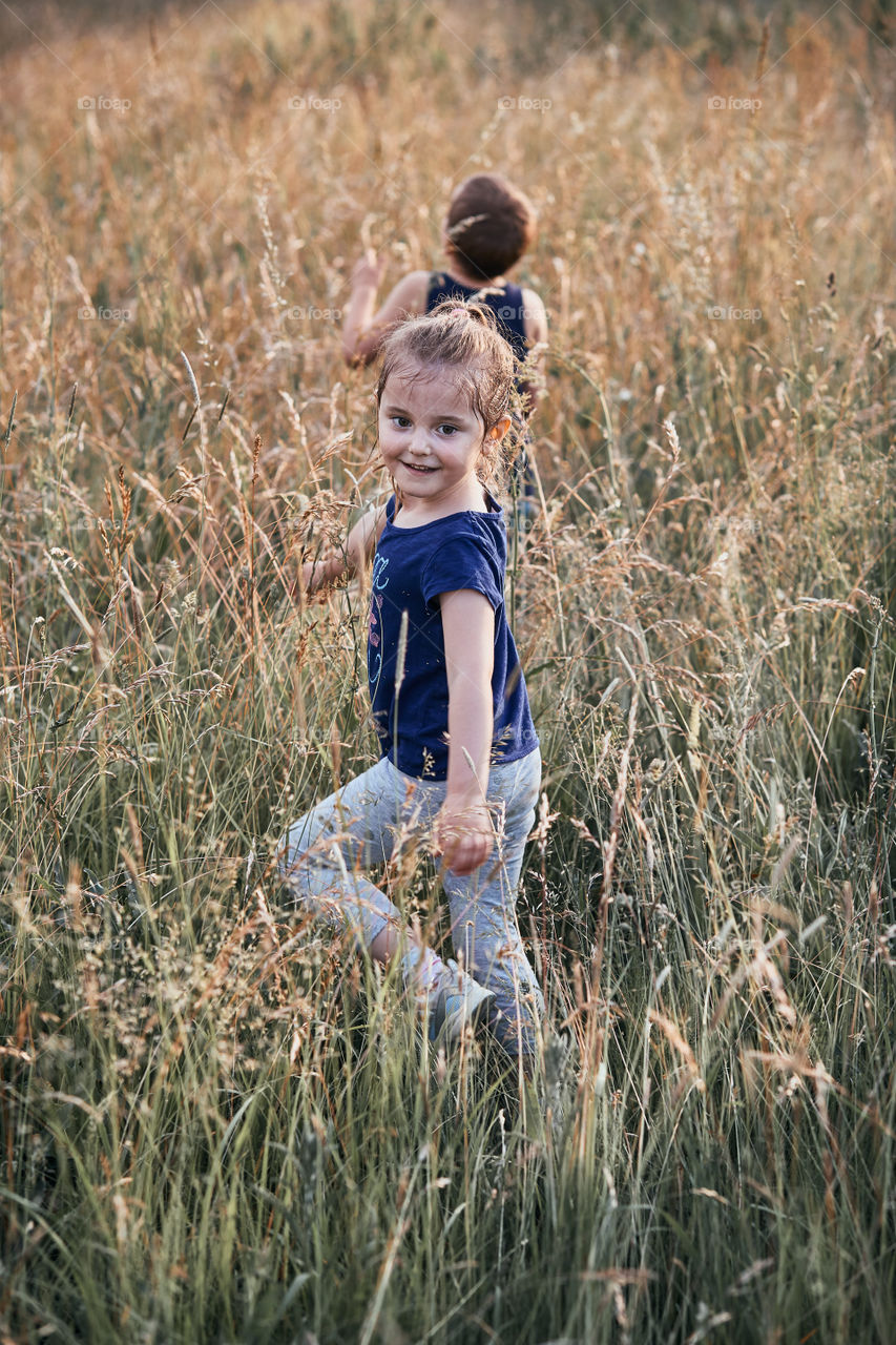 Little happy smiling kids playing in a tall grass in the countryside. Candid people, real moments, authentic situations