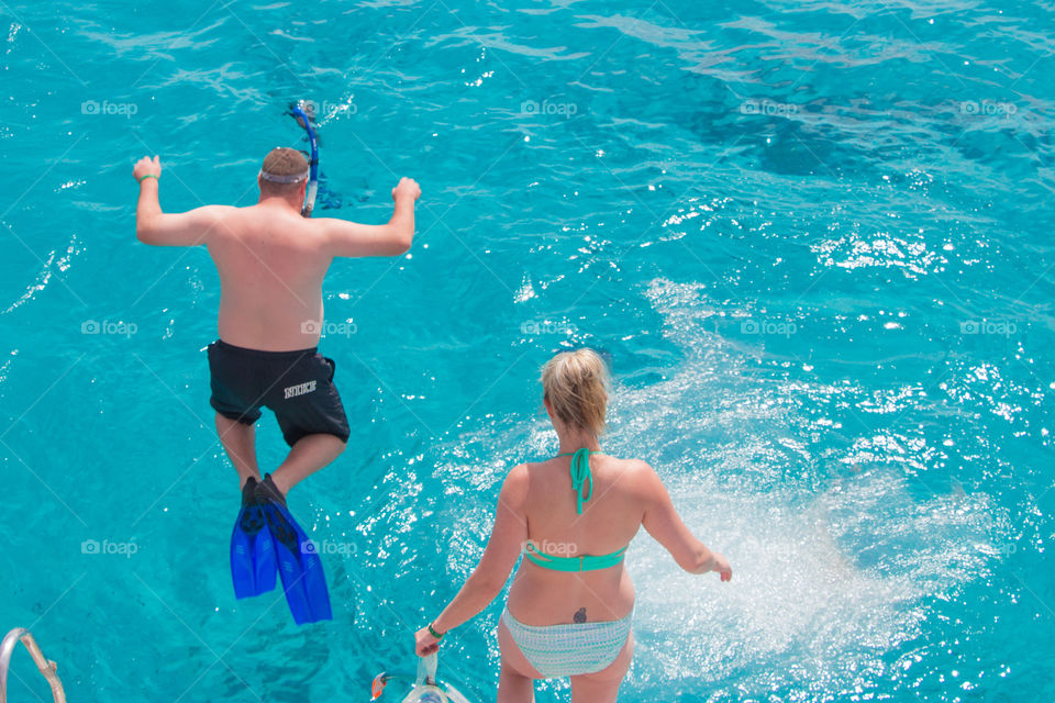 Two people jumping off the boat going for a snorkel