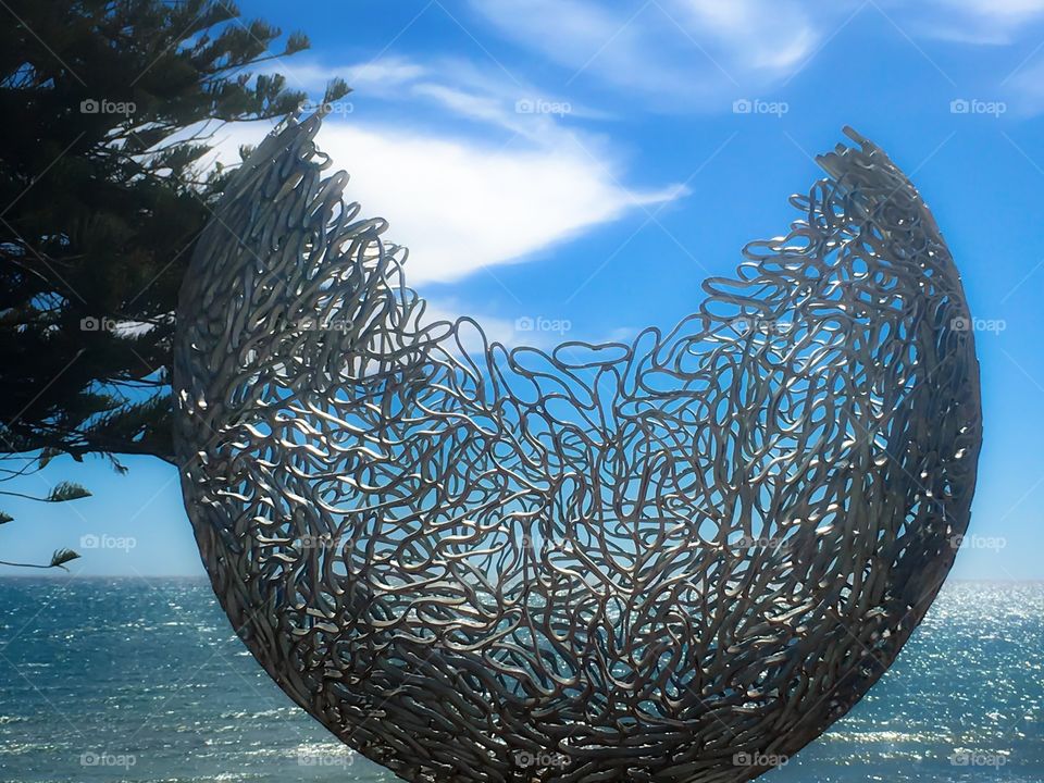 Beautifully rendered metal steel grey structure sculpture against the backdrop of ocean and blue sky 