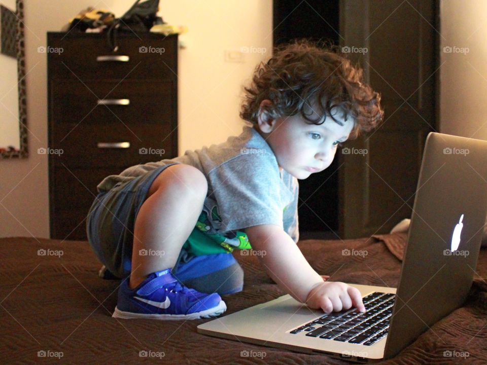 Toddler boy using laptop on bed