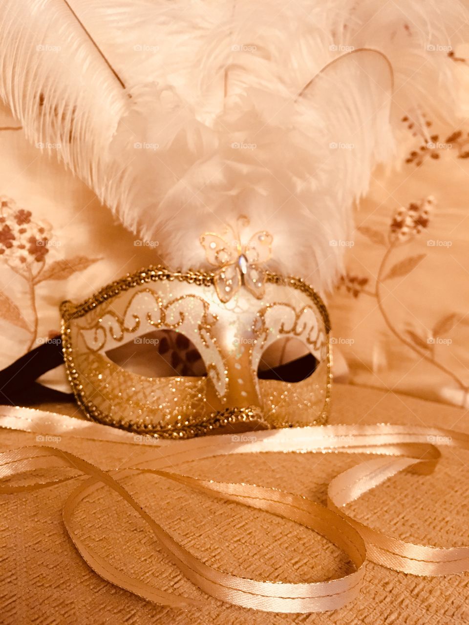 Gold Venetian masquerade mask with white feathers and gold ribbon swirled in the foreground 