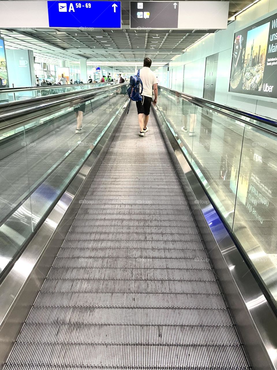 Man walking on the long escalator at the airport heading towards the gate, going on vacation 