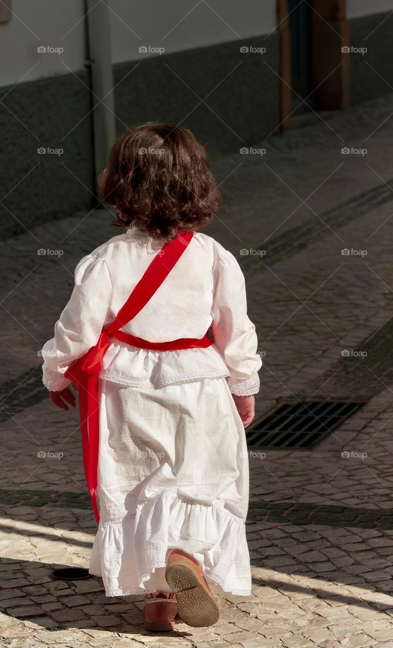 Little girl in white dress with a red sash