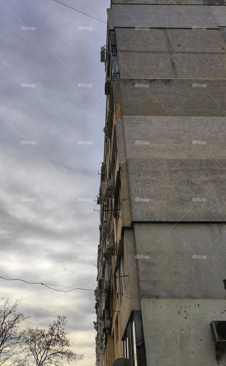 A photo of an old panel apartment building in a neighbourhood in Bulgaria in neutral colours and a cloudy sky