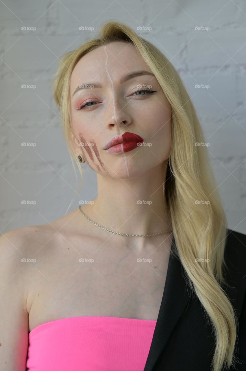 Close-up portrait of a blonde girl look at camera with different make-up on half of her face on white background