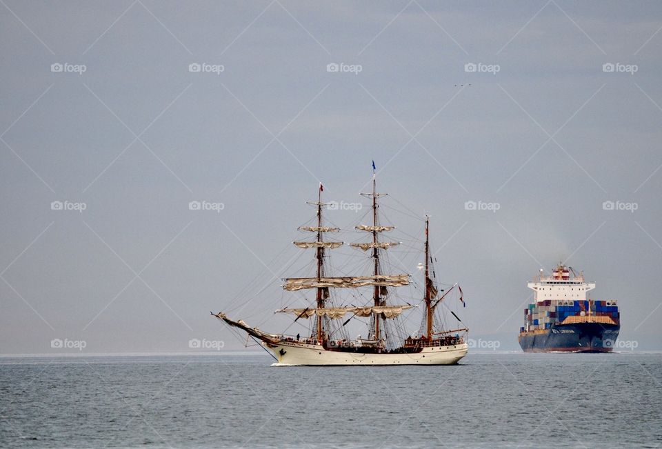 A very old Sailing ship with a modern cargo ship behind. "The old and the new"