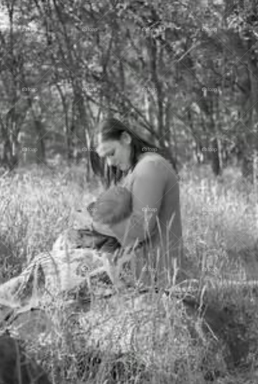 A mother breastfeeds her son outside in nature. Grass and trees are a relaxing backdrop to this tender moment. 