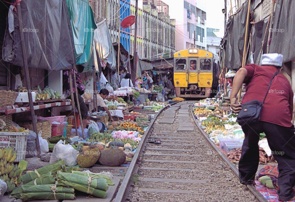 A passenger train is running through the middle of the famous Maeklong Railway Market or folding umbrella market as the awnings, vegetables and fruits are pulled back only as far as necessary and once the train passes through (six times a day) everything returns to normal.