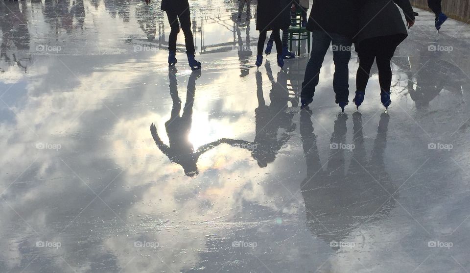 Reflection of ice skaters, holding hands with sun beaming off the ice