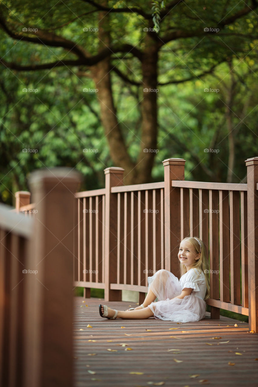 Happy little girl with blonde hair sitting in park