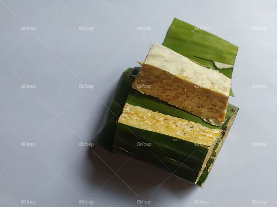 Tempe or tempeh wrapped in banana leaves, is a traditional Indonesian food. made of fermented soybeans on an isolated white background