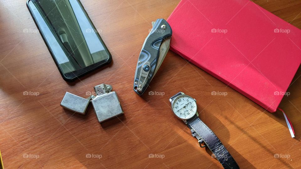 Pobeda men's watch, red notepad, folding knife, petrol zipo lighter and smartphone on the table