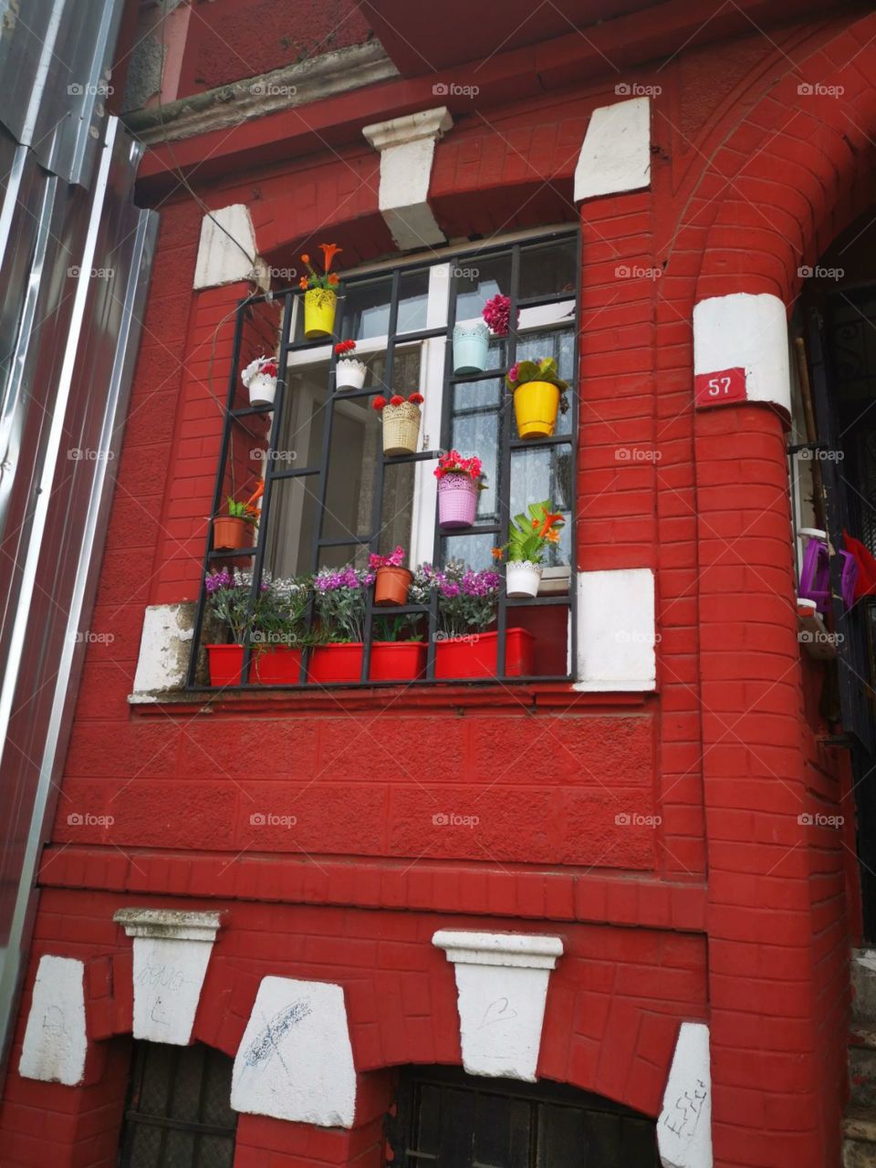 A nice house with seeable red and white bricks. An interesting set up vases with flowers on the iron cage before the window.