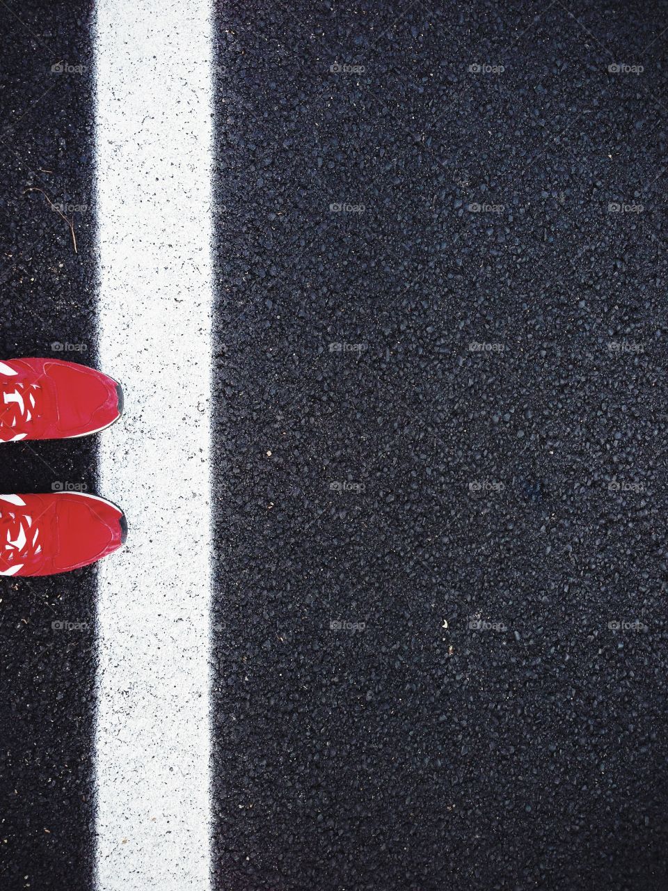 A pair of mans ted shoes standing over a black asphalt road, touching the white stripe with the tip.