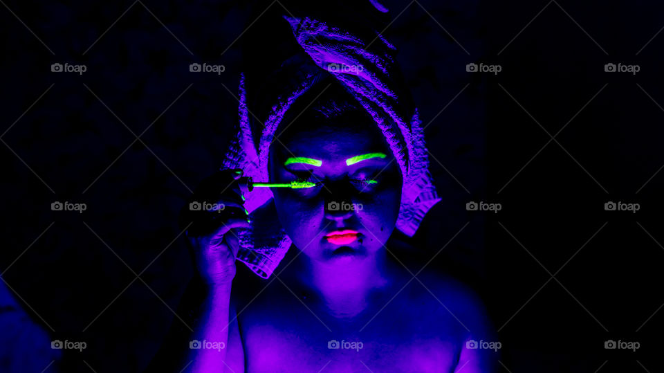 The girl was bathing in the shower and put a towel on her head to dry her hair, dyes her eyelashes with mascara in neon color, neon make-up