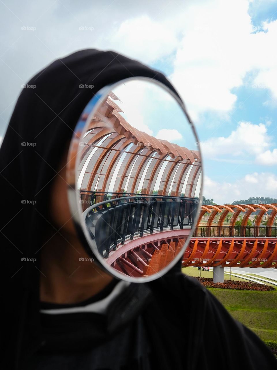 A portrait of a man wearing a hoodie with a mirror on his face to reflect the beautiful pedestrian crossing bridge