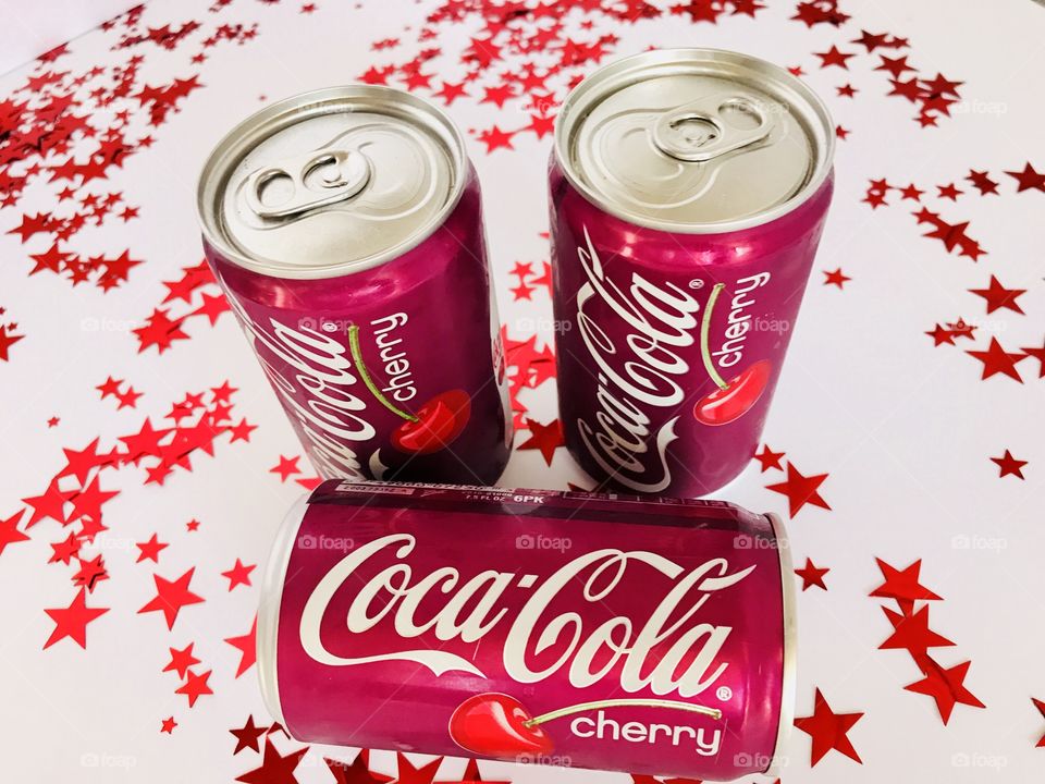 Three cans of Cherry Coca-Cola on a white background with red stars