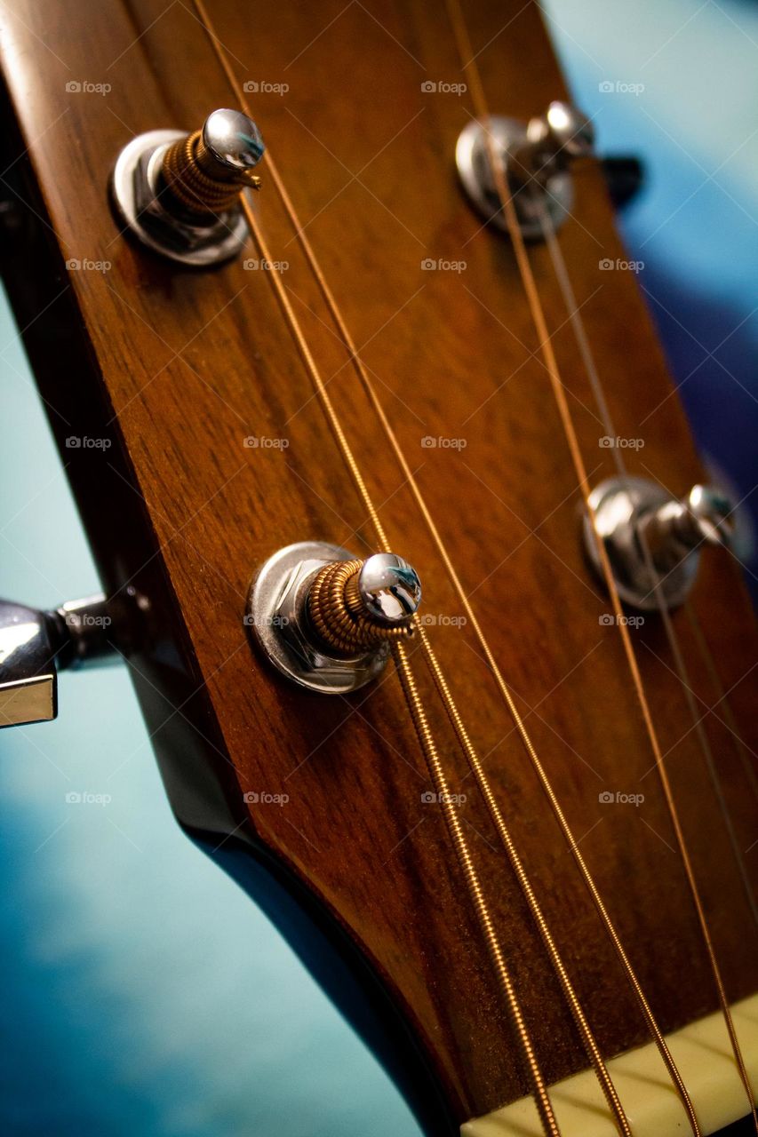 A deeply warm wooden acoustic guitar head with silver tuning knobs and steel strings.