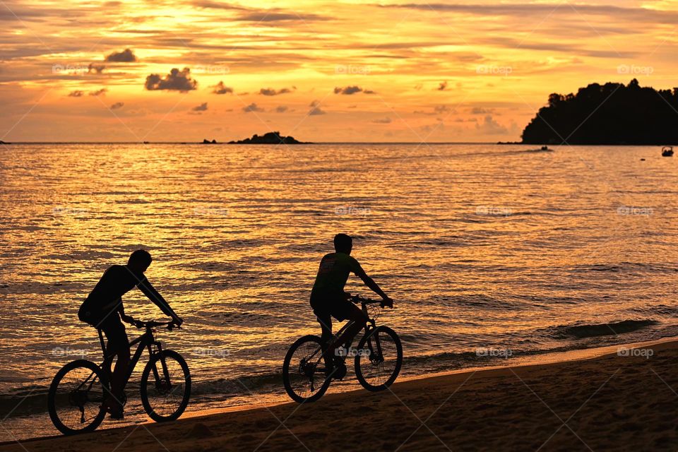 Couple ride a bicycle along the beach at sunset
