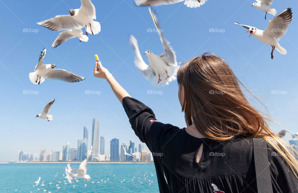 Young woman feeding seagulls at the beach in the city