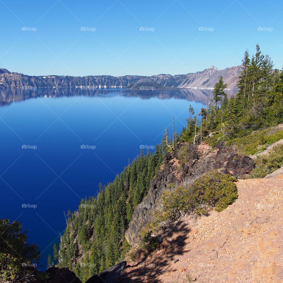 Wizard Island reflecting in the rich blue waters of Crater Lake in the forests of Southern Oregon on a sunny summer morning. 