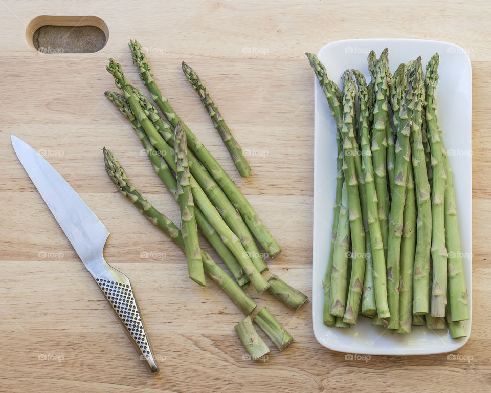 Fresh asparagus on a cutting board with a sharp knife.