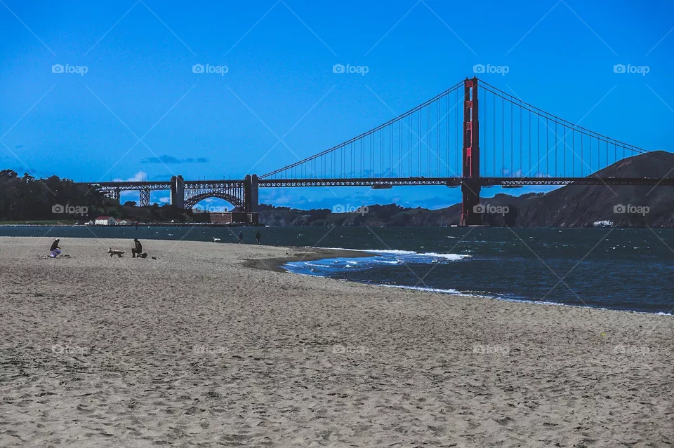 Looking down the beach at Crissy Field in San Francisco California at the Golden Gate Bridge on a warm sunny afternoon with clear blue skies, and you can see Fort Point in the distance 