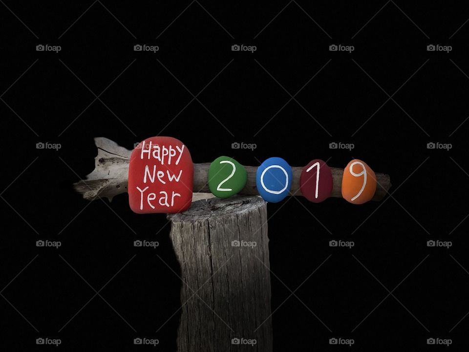 Happy New Year with colored stones on a wooden pole and black background