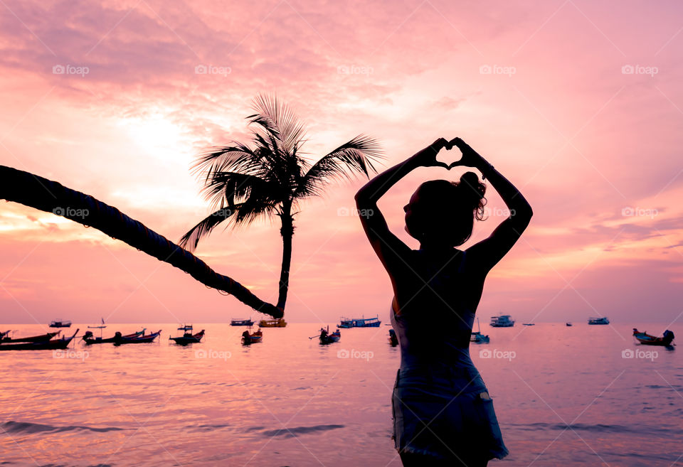 Silhouette of woman making heart shape at beach during sunset