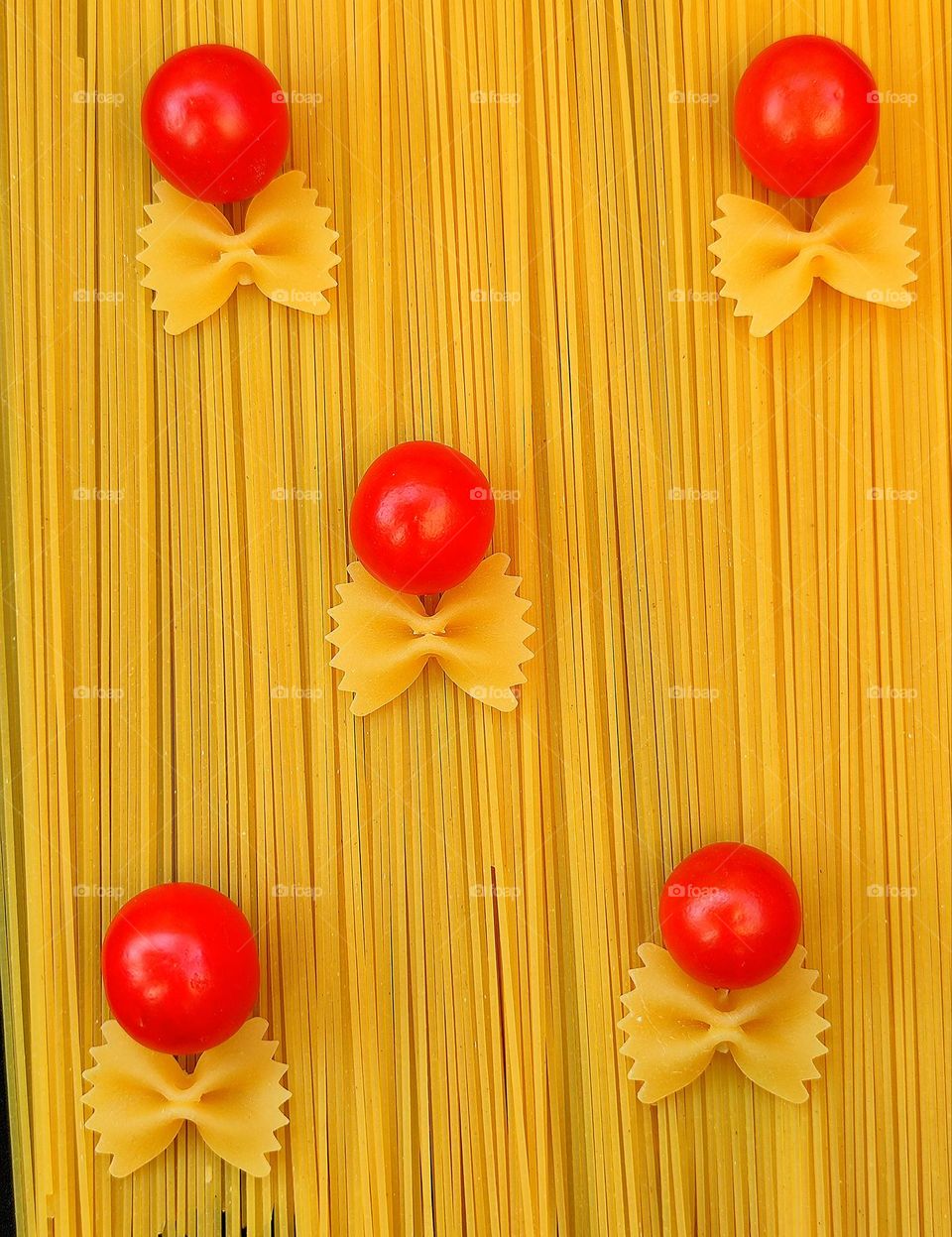 Pasta colors and shapes. Farfalle-shaped pasta and red tomatoes lie on spaghetti. Yellow explosion of various pasta and red spots of tomatoes