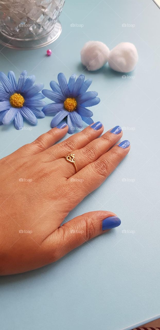 gold ring to middle finger along with blue nail polish and blue flowers