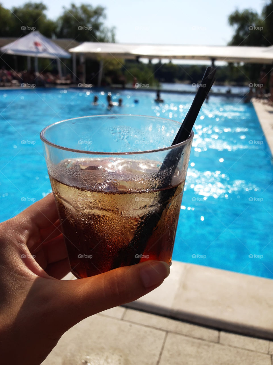 Summer relax with glass of cola near blue swimming pool 