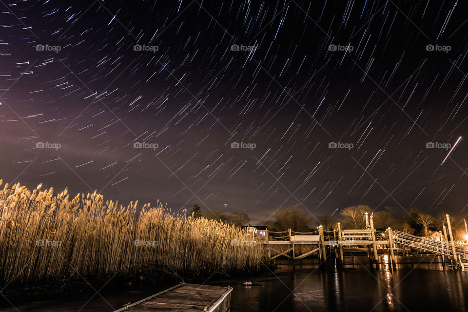 Star trails over a dock and some beach grass.