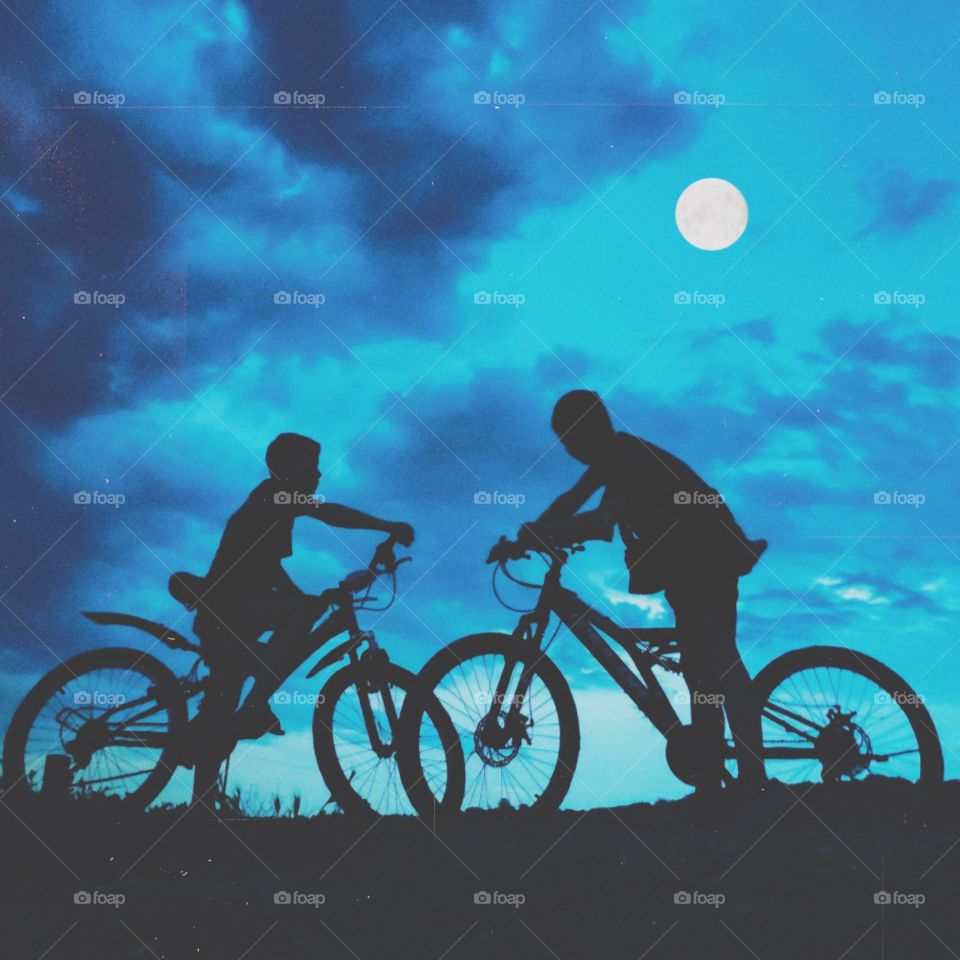 Silhouettes of boys on bicycle.