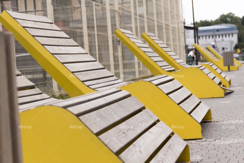 A modern, wooden bench with yellow edges in a metropolitan area.  A corner of peace and tranquility.