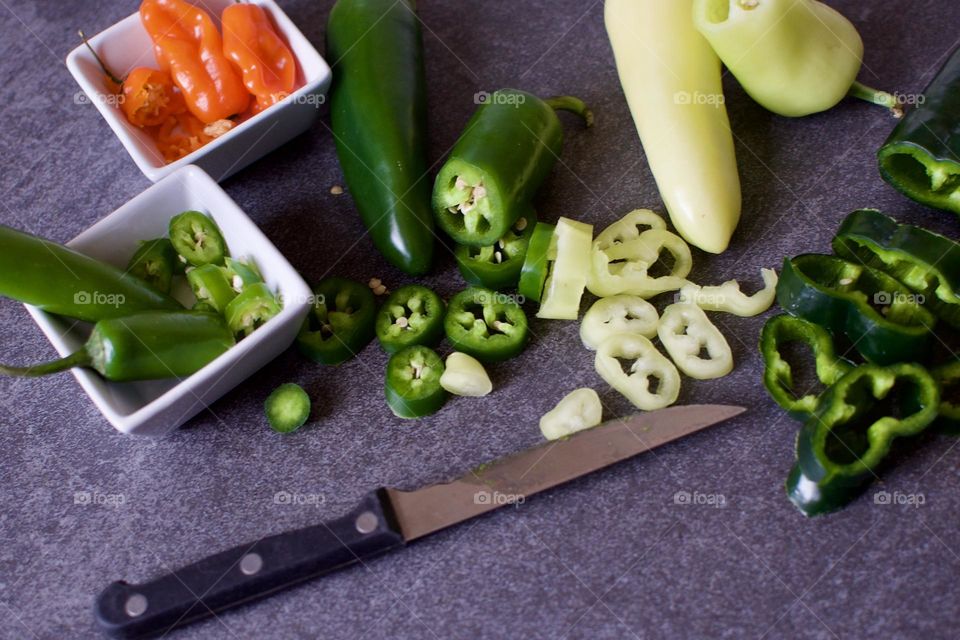 Fresh cut variety of spicy peppers and a knife on a slate background 