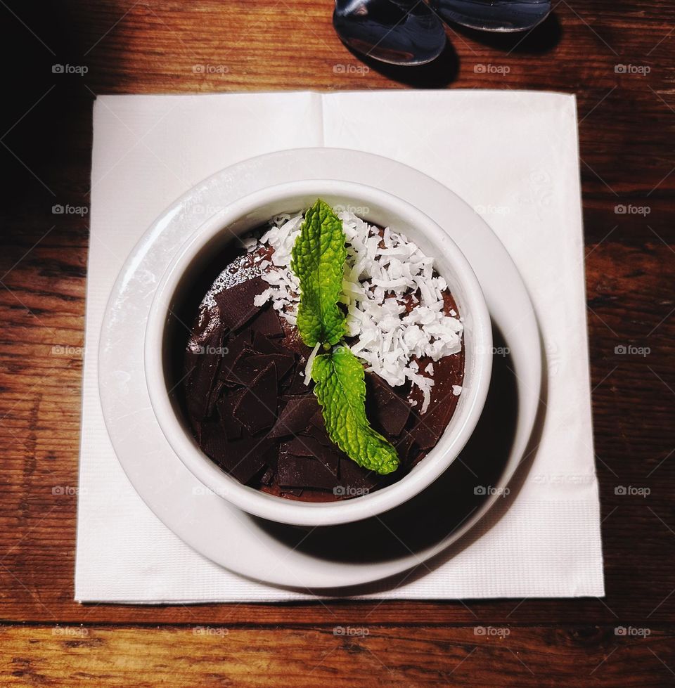 Delicious chocolate pudding with coconut flakes and chocolate chunks toppings on a white small cup. 