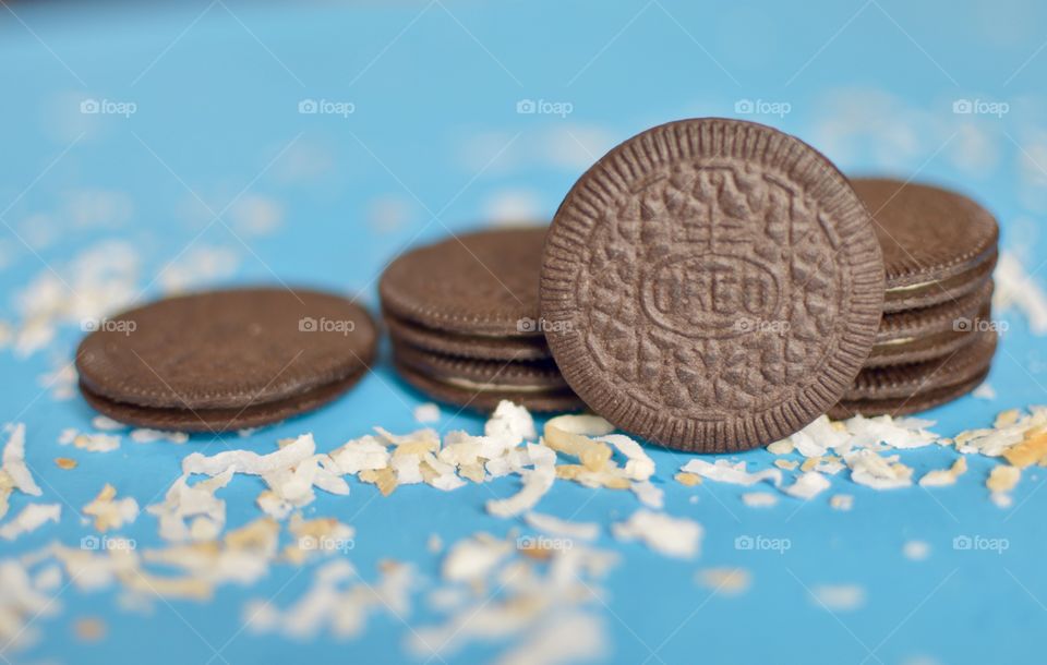 A stack of coconut Oreo thin cookies on a blue background with coconut shreds