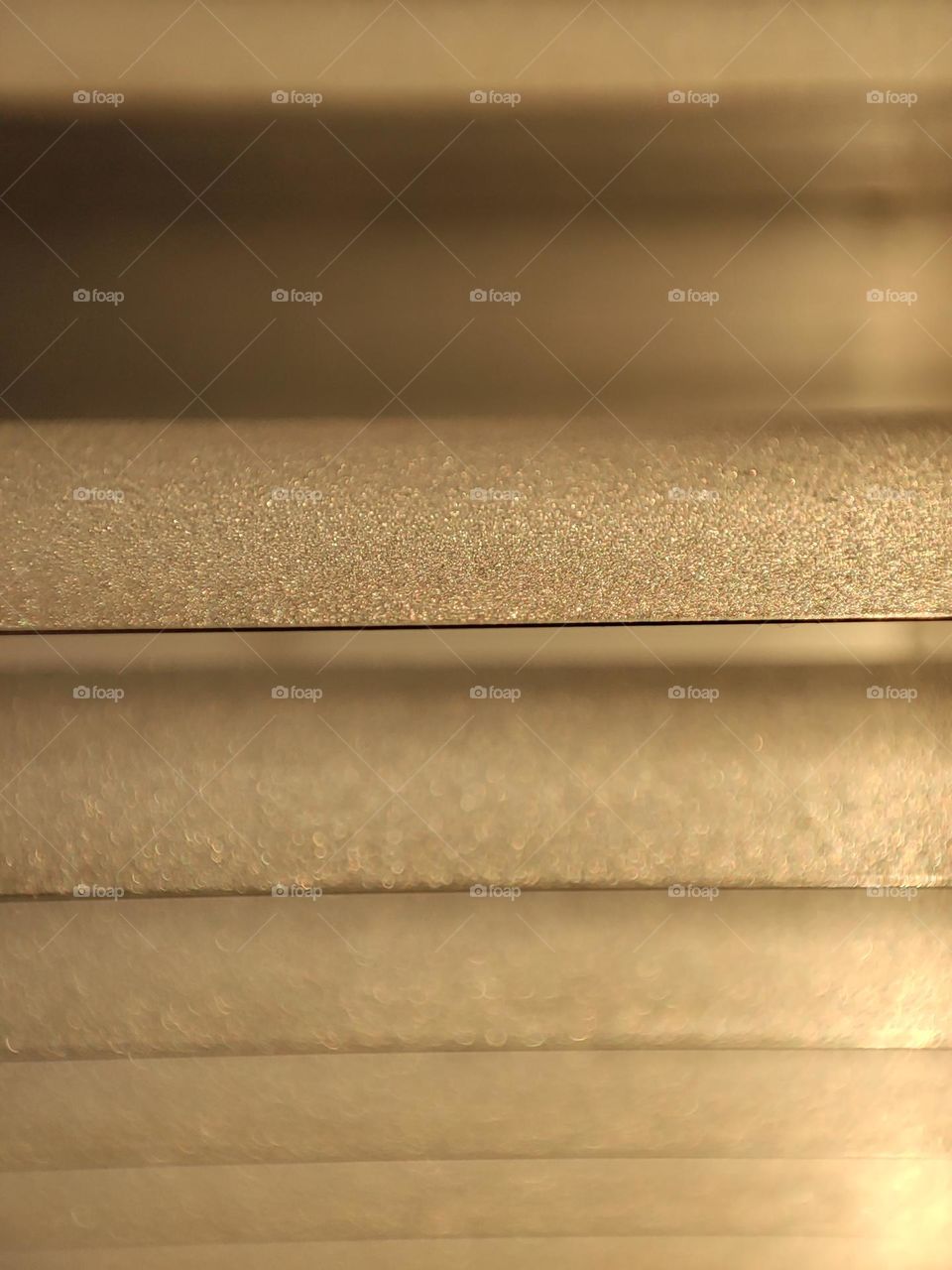 A macro photo of window blinds in the golden hour with dust on them