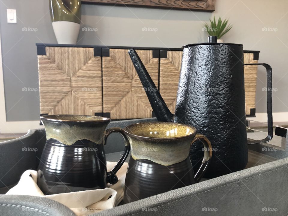 A black teapot and ceramic teacups on a coffee table in a bedroom 