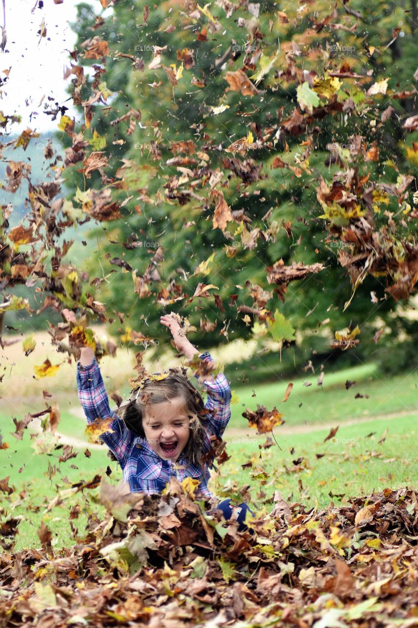 child jumping in the leaves and throwing them