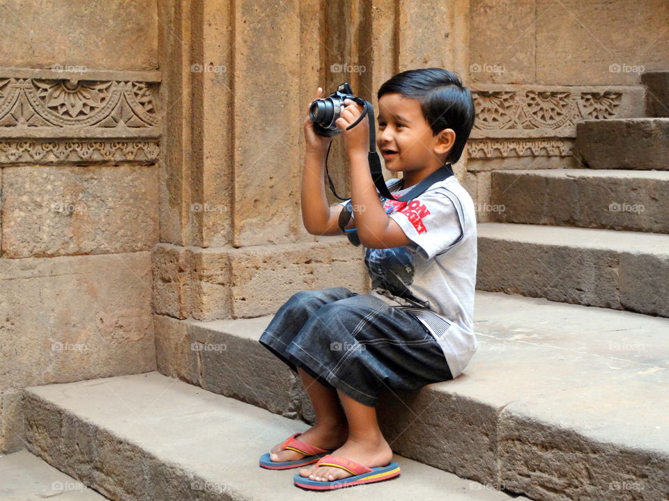 A little boy sitting on stair and photographing with camera