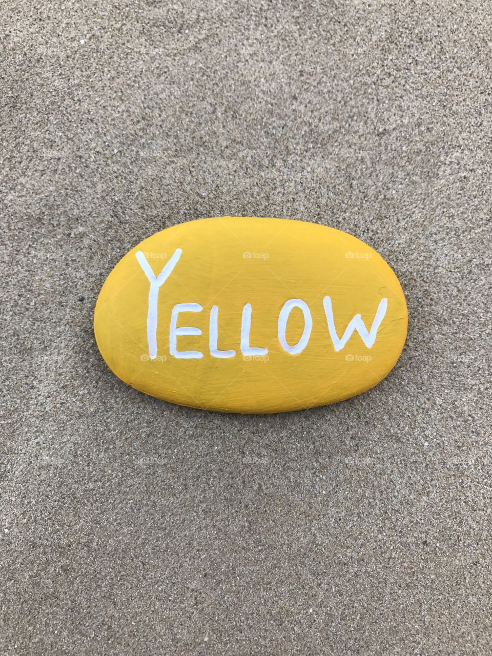 Yellow painted stone on the sand 