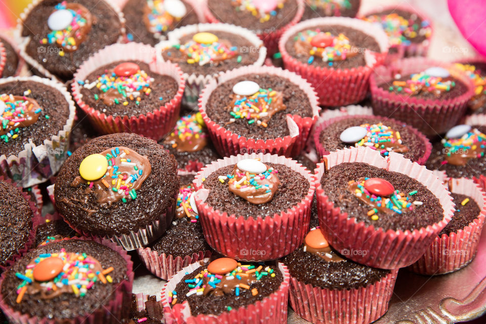 Tasty handmade freshly baked cacao chocolate muffins with cream and colorful toppings, arranged on tray.