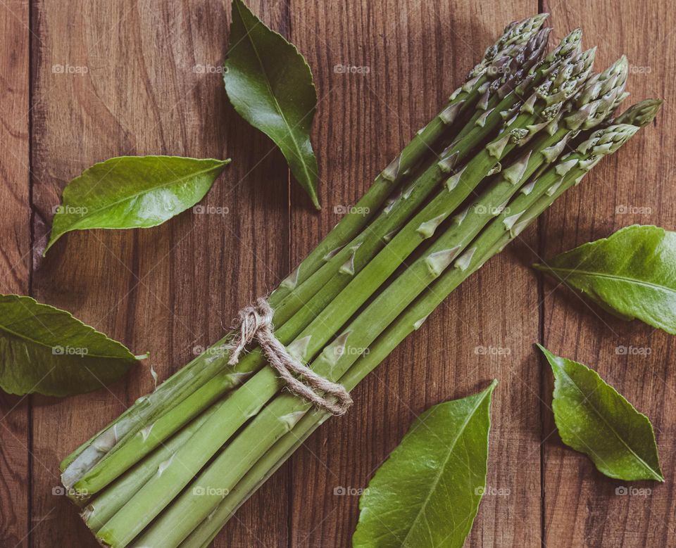 A bunch of asparagus spears on a wood background with lemon tree leaves