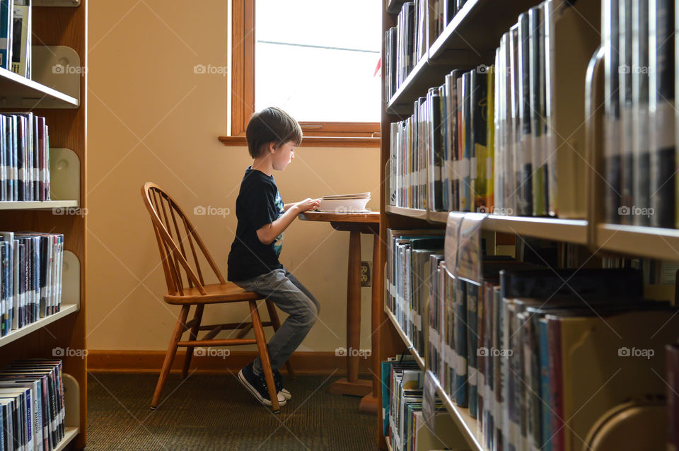 Young boy reading a book at a table in a library