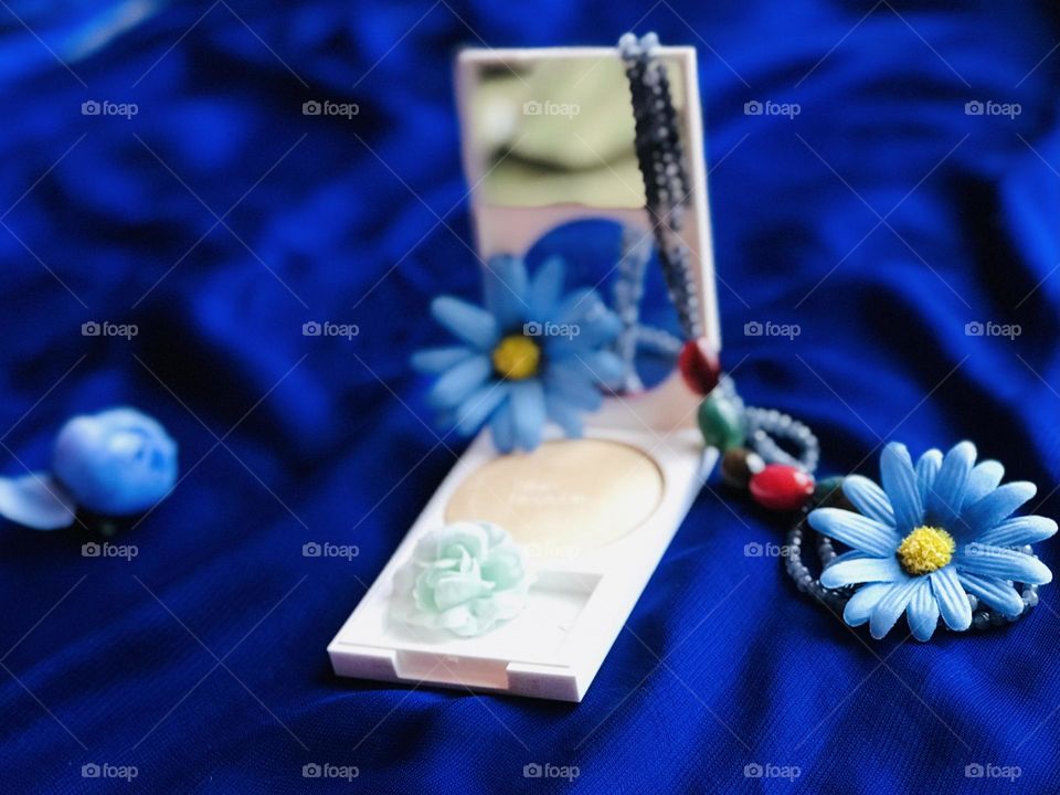 a beauty product with blue flowers and pearl chain placed on blue satin cloth 