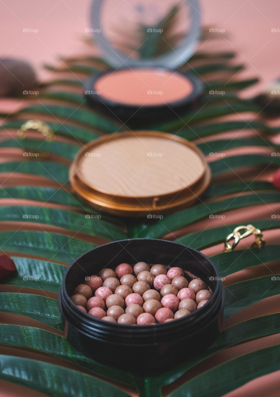 Set of three pieces of nude tonal facial powders granular lying on a palm tree on a pink background,side view. Concept female cosmetics, beauty salon.