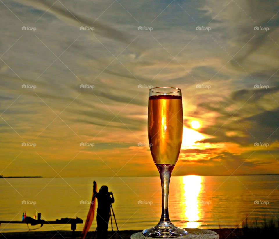 Liquids - A colorful glass of wine while watching a photographer takes sunset photos as the golden sun descends below the horizon