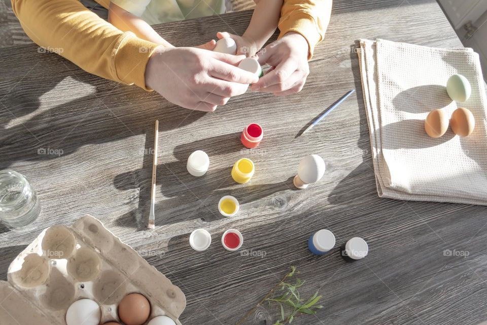 Dad teaches a small child to draw with bright, multi-colored gouache paints on a gray, wooden table